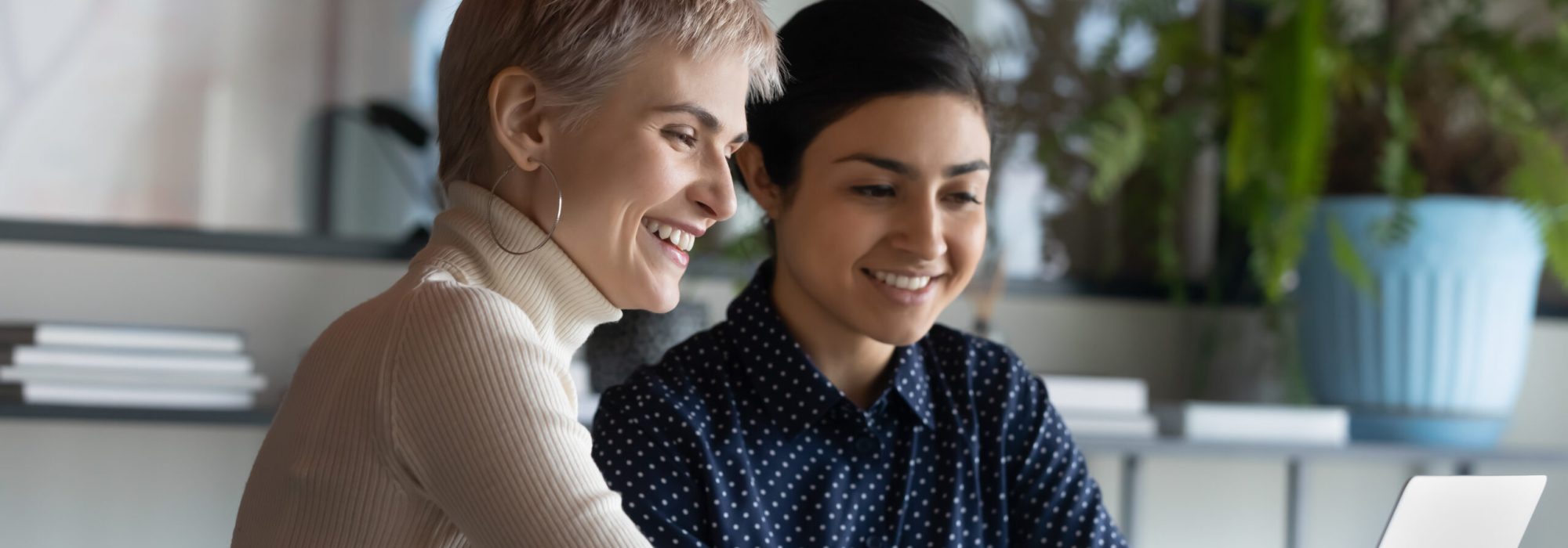 Caucasian short-haired woman contact with Indian colleague international department company staff members working together use laptop, take break use internet browse web have fun at workplace concept